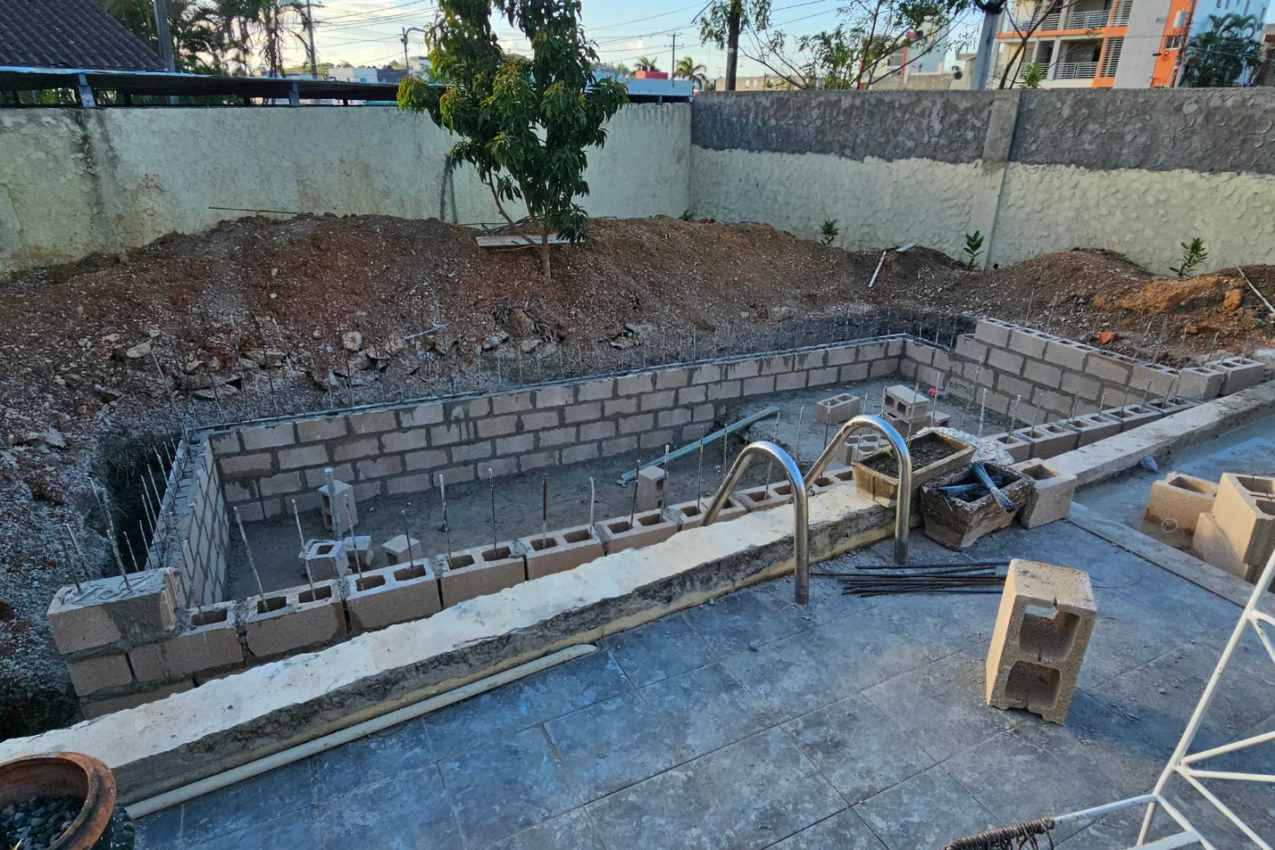 Piscina en construcción con muros de bloques y terreno excavado alrededor.