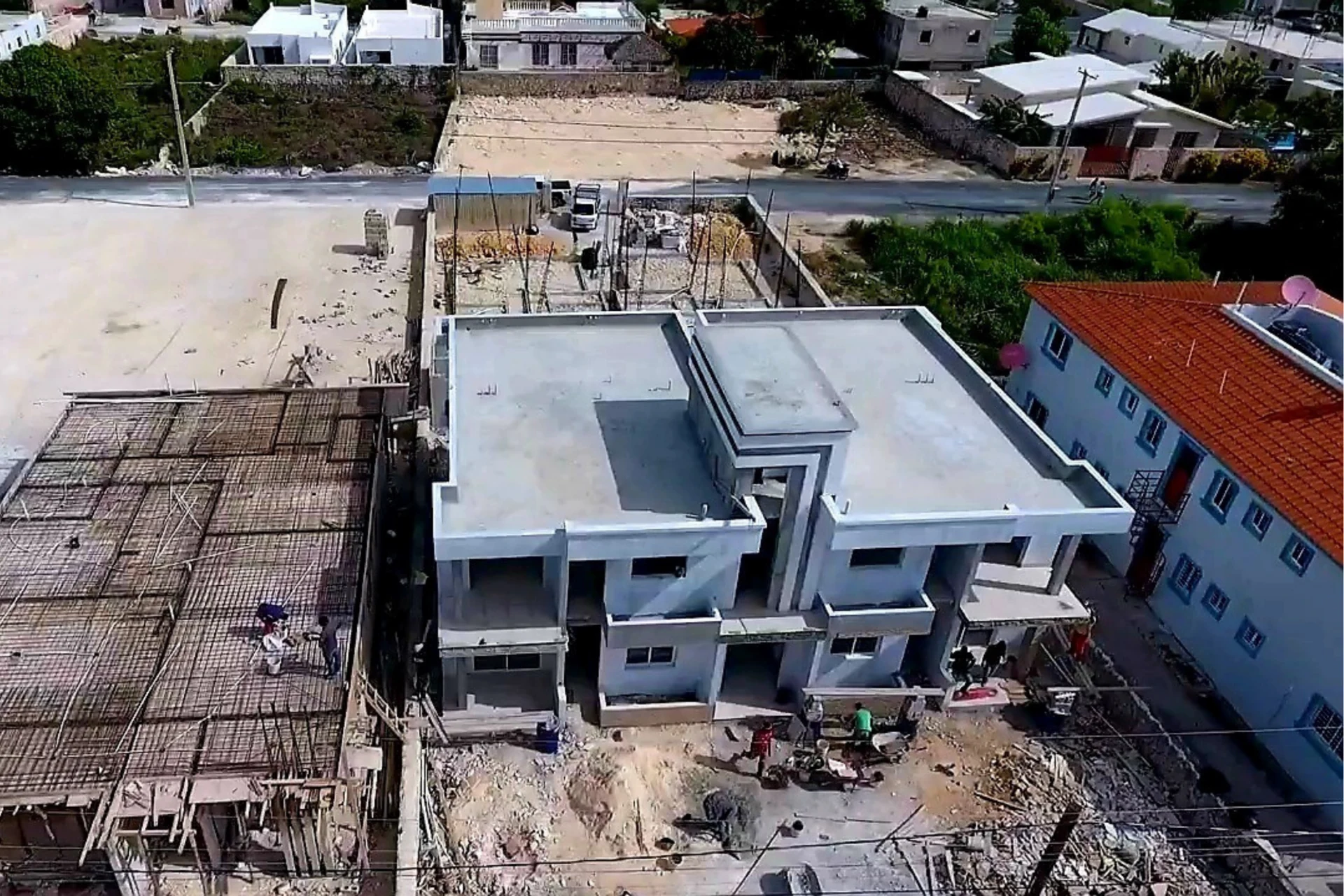 Vista aérea frontal de un edificio de cubierta plana junto a una superficie con entramado y personas.