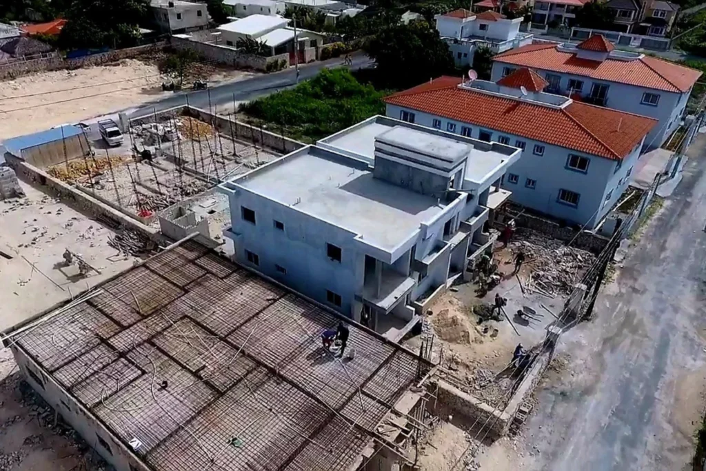 Vista aérea oblicua de un edificio de cubierta plana entre una superficie con entramado y casas de tejados rojos.