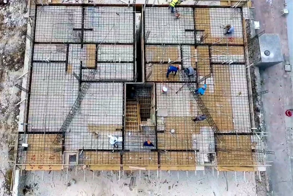 Vista cenital de una superficie cubierta por una cuadrícula de varillas, con varias personas y un hueco central.