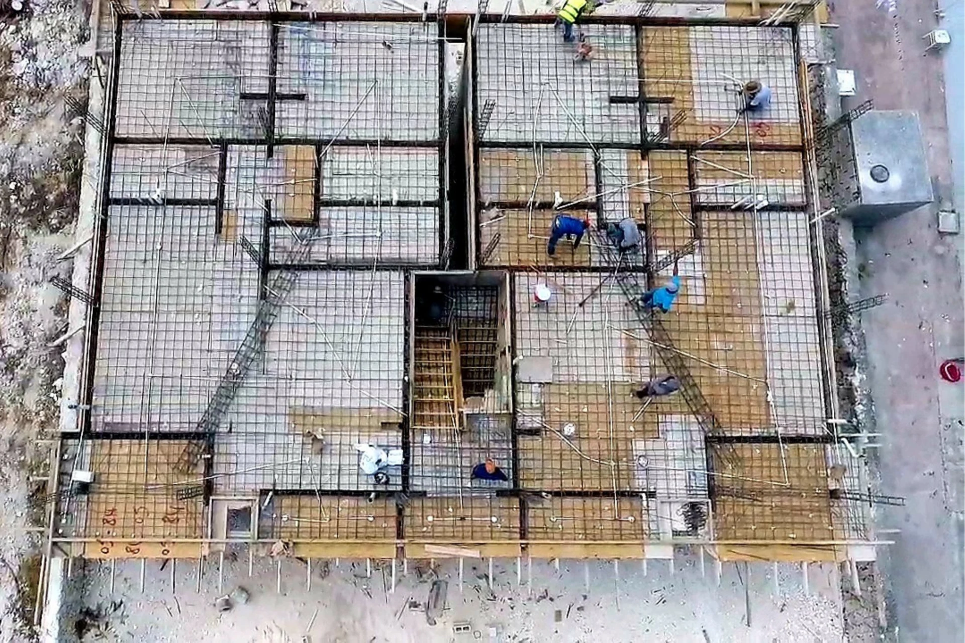 Vista cenital de una superficie cubierta por una cuadrícula de varillas, con varias personas y un hueco central.