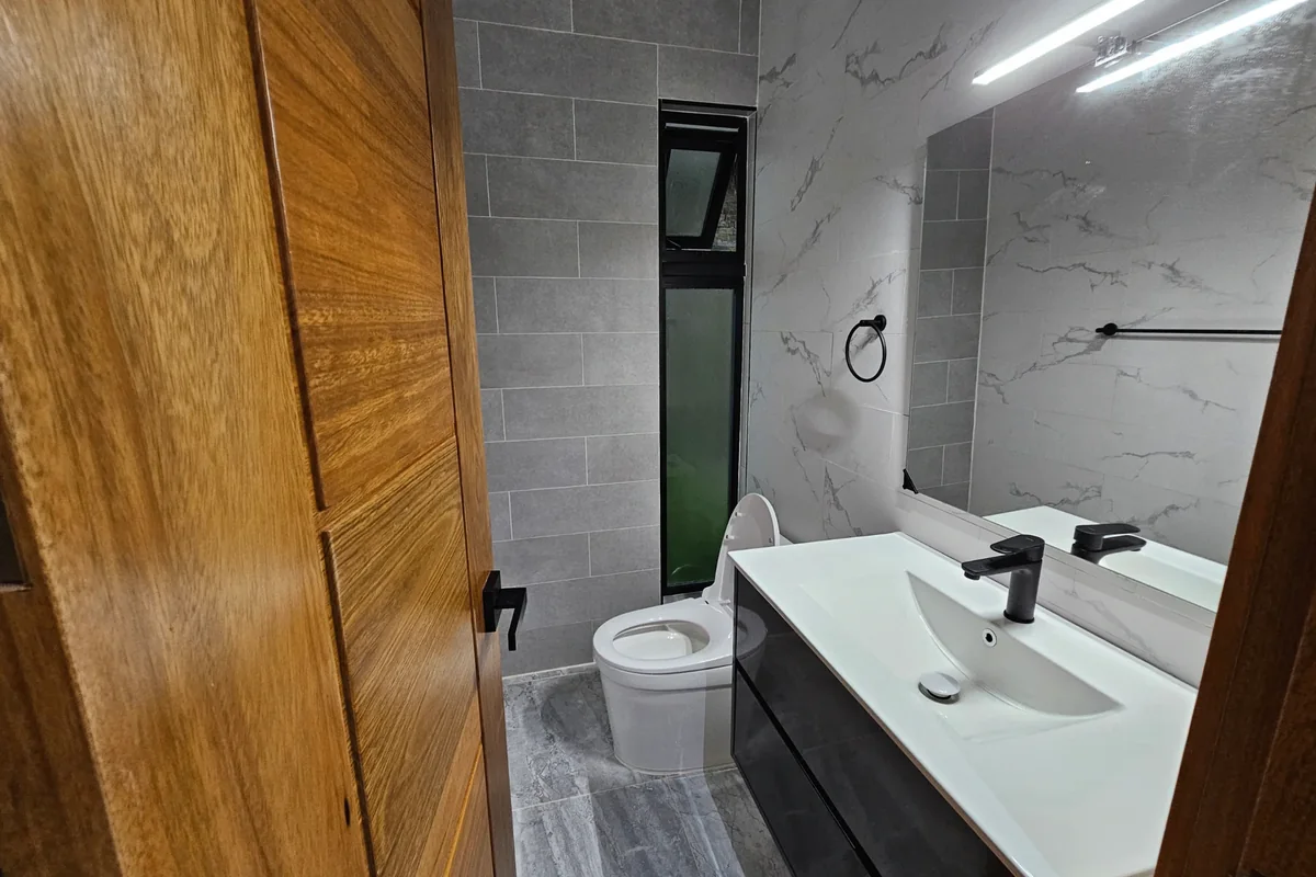Baño de Nain Luxury, con lavabo blanco, grifo negro y ventana vertical.