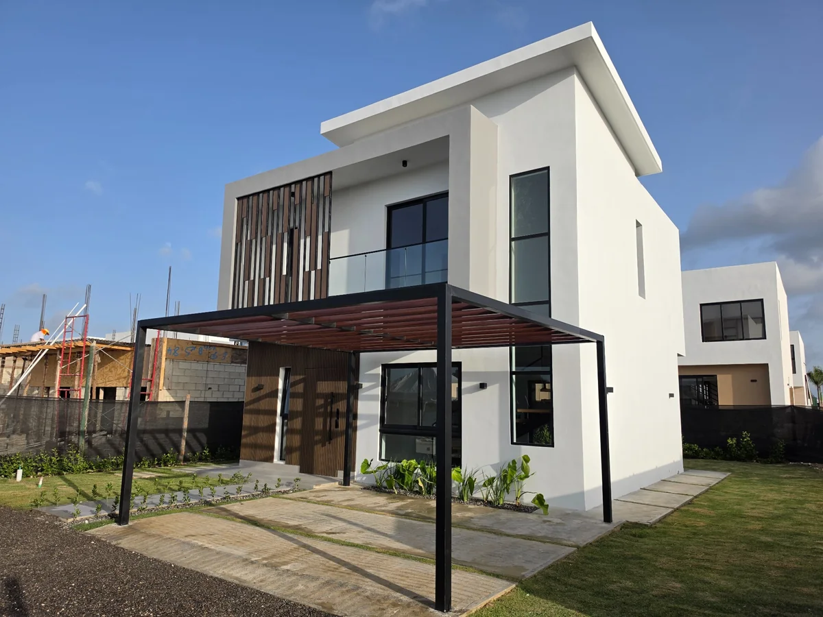 Villa Sunlax construida, con fachada blanca, balcón y pérgola de estacionamiento.